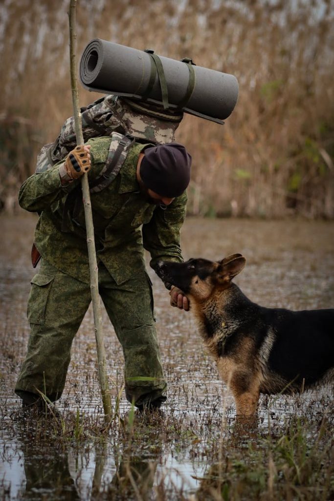 A man in camouflage with a German Shepherd on a swamp hike in Astara, showcasing adventure and companionship.