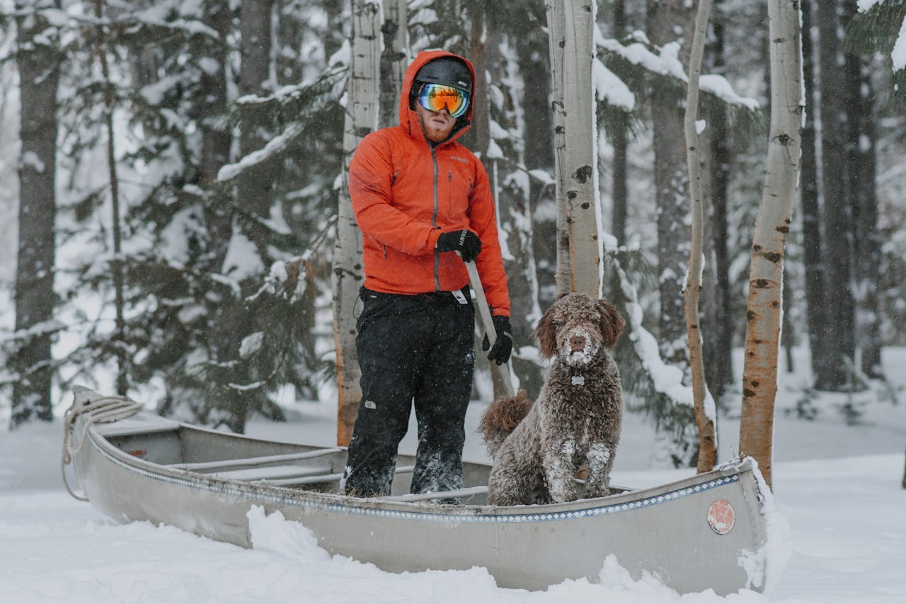 A man with his dog in a canoe amidst a snowy forest landscape, evoking winter adventure.